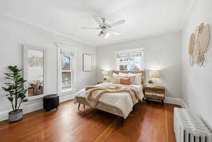 Bedroom with radiator heating unit, ornamental molding, wood-type flooring, and ceiling fan