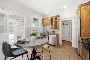 Kitchen with glass insert cabinets, stainless steel appliances, dark countertops, wood finish cabinets, and ornamental molding