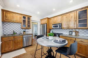 Kitchen with glass fronted cabinets, stainless steel appliances, wood finish cabinets, light tile patterned floors, and ornamental molding