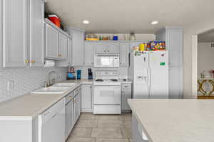 Kitchen featuring white appliances, light countertops, decorative backsplash, light tile patterned floors, and a textured ceiling