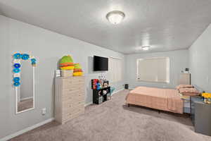 Carpeted bedroom featuring baseboards and a textured ceiling