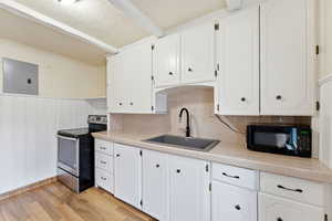 Kitchen featuring tile countertops, electric range, white cabinetry, a wainscoted wall, and a textured ceiling