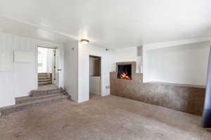 Unfurnished living room featuring carpet floors and a lit fireplace