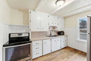 Kitchen with a wainscoted wall, stainless steel appliances, tile counters, light wood finished floors, and white cabinetry