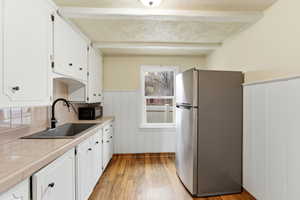 Kitchen featuring tile counters, freestanding refrigerator, light wood-style flooring, white cabinets, and wainscoting