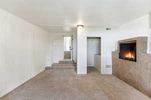 Unfurnished living room with a textured ceiling, carpet flooring, and a tiled fireplace