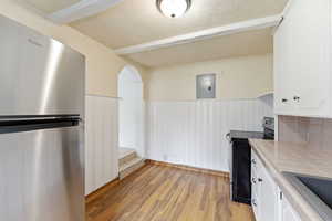 Kitchen featuring freestanding refrigerator, tile countertops, white cabinets, a textured ceiling, and a wainscoted wall