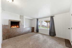 Unfurnished living room with carpet flooring, a fireplace, and a textured ceiling