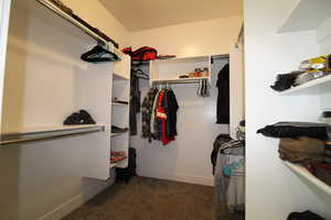 Walk-in closet featuring dark colored carpet and plenty of storage