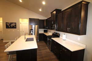 Kitchen with stainless steel appliances, dark wood finish cabinets, an island with sink, dark wood-style floors, and a breakfast bar