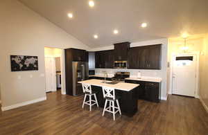 Kitchen with stainless steel appliances, dark wood finish cabinets, an island with sink, dark wood-style floors, and a breakfast bar
