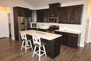 Kitchen with stainless steel appliances, dark wood finish cabinets, an island with sink, dark wood-style floors, and a breakfast bar