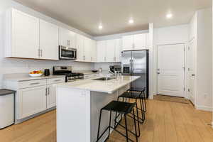 Kitchen featuring an island with sink, a kitchen breakfast bar, stainless steel appliances, white cabinetry, and light wood-style floors