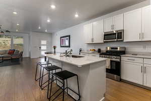 Kitchen with stainless steel appliances, open floor plan, a kitchen bar, a kitchen island with sink, and light stone counters