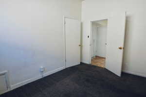 Unfurnished bedroom featuring baseboards and dark carpet