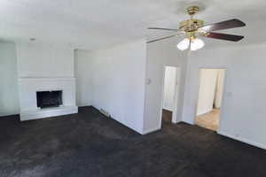 Unfurnished living room with dark colored carpet, a textured ceiling, ceiling fan, and a brick fireplace