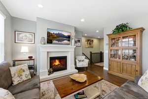 Living room with dark wood-type flooring, a glass covered fireplace, and recessed lighting