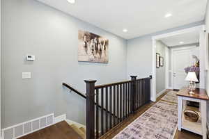 Hall featuring an upstairs landing, dark wood-style floors, and recessed lighting