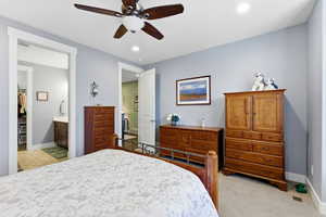 Bedroom with light colored carpet, a ceiling fan, recessed lighting, connected bathroom, and a spacious closet