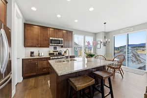 Kitchen with light stone countertops, stainless steel appliances, dark wood-type flooring, suspended lighting, and a center island with sink
