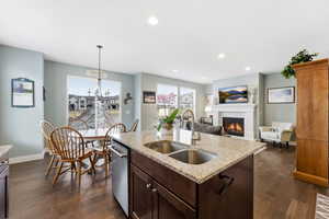 Kitchen featuring dark wood finish cabinetry, light stone countertops, a glass covered fireplace, and a kitchen island with sink
