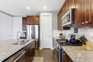Kitchen featuring stainless steel appliances, dark wood-type flooring, light stone counters, backsplash, and recessed lighting