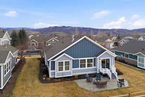 Rear view of property featuring board and batten siding, a residential view, a patio area, a mountain view, and a yard