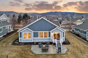 Rear view of property featuring a patio, board and batten siding, an outdoor living space with a fire pit, a mountain view, and a lawn