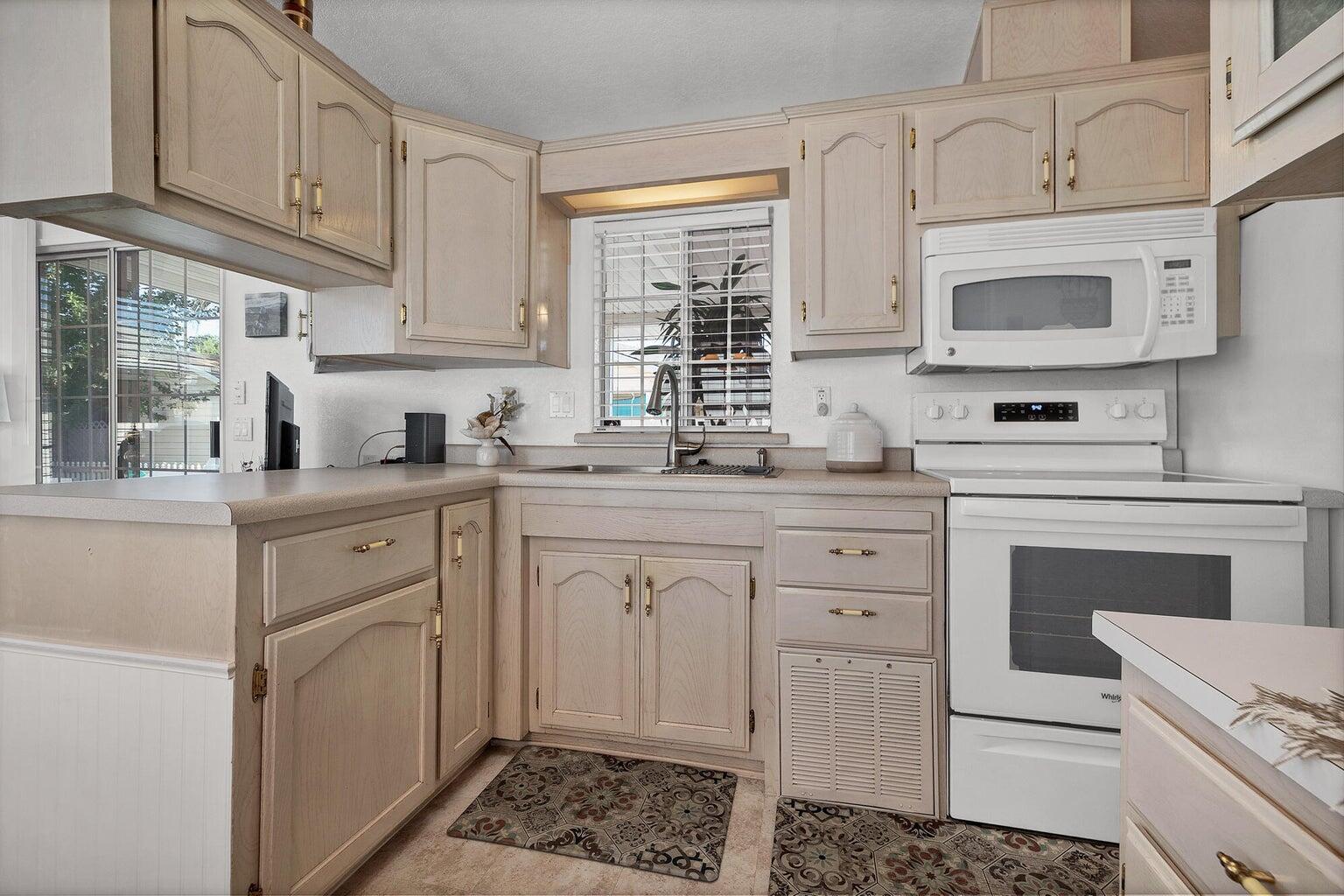 Kitchen featuring neutral cabinetry, a white appliance suite, light countertops, and a window with blinds