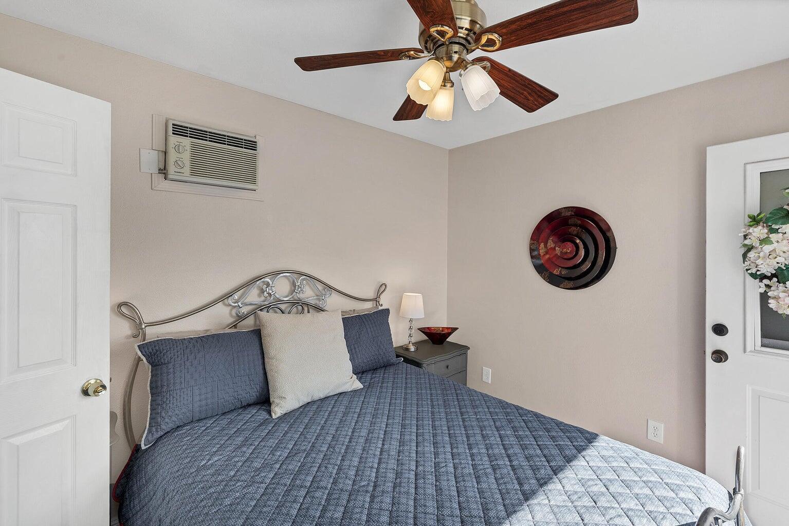 Bedroom featuring a decorative metal headboard, wall-mounted air conditioning unit, and a ceiling fan with integrated lighting