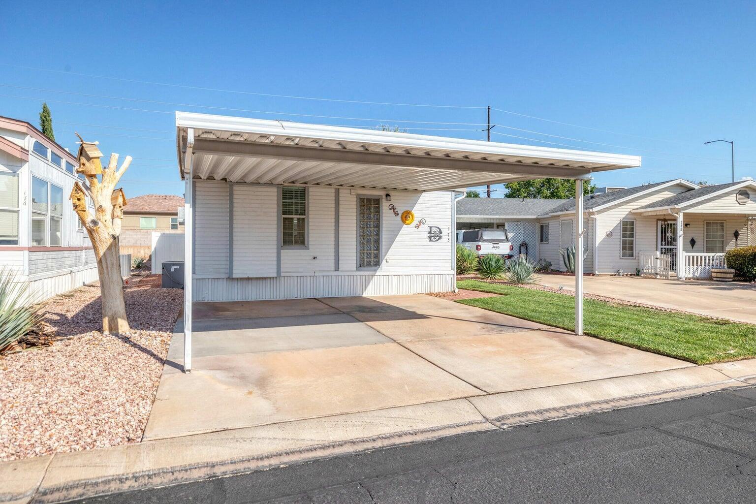 Exterior featuring white horizontal siding, a covered carport, concrete driveway, decorative glass block window, and xeriscape landscaping