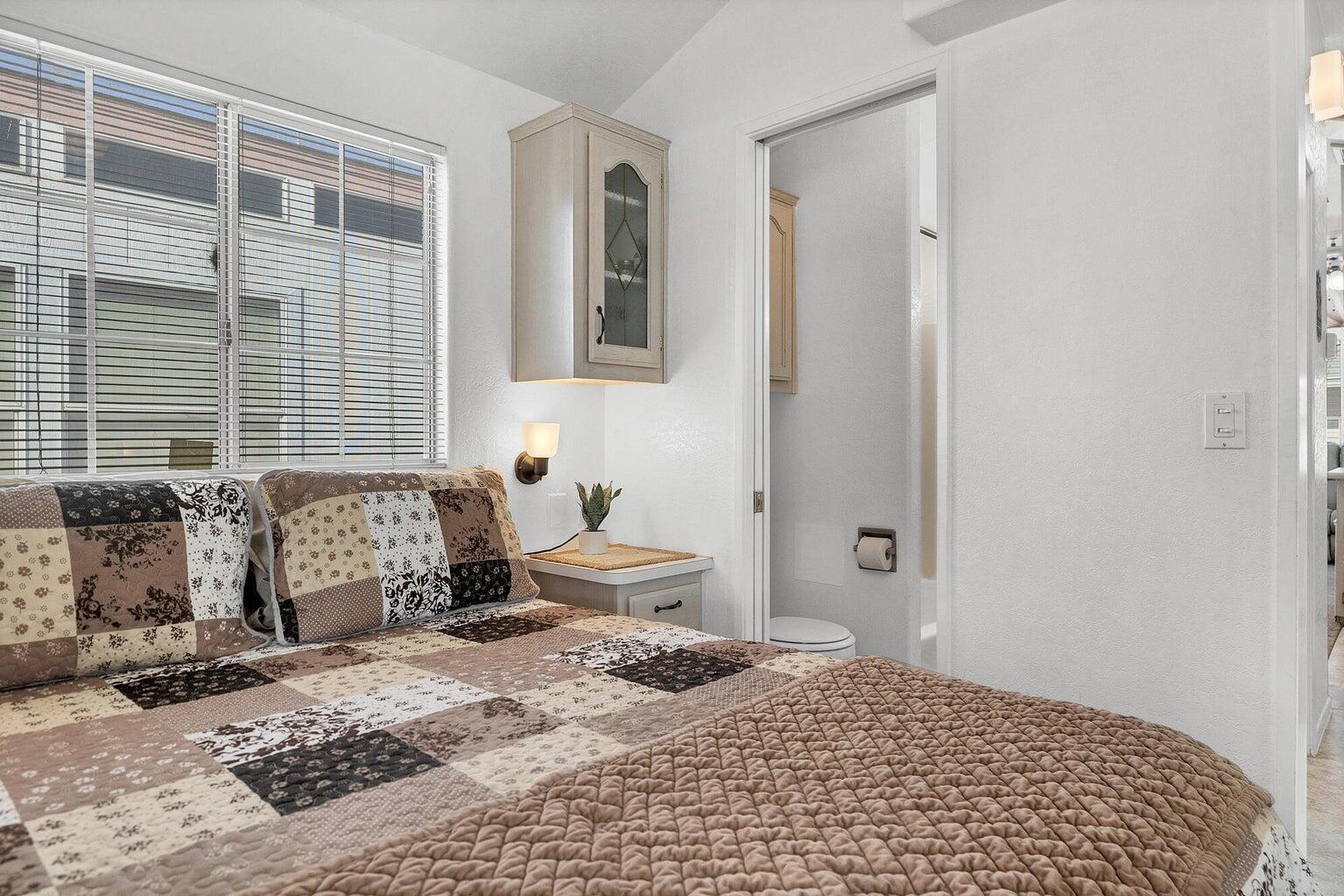 Bedroom featuring a window with horizontal blinds, overhead cabinetry with glass inserts, and a wall-mounted light fixture