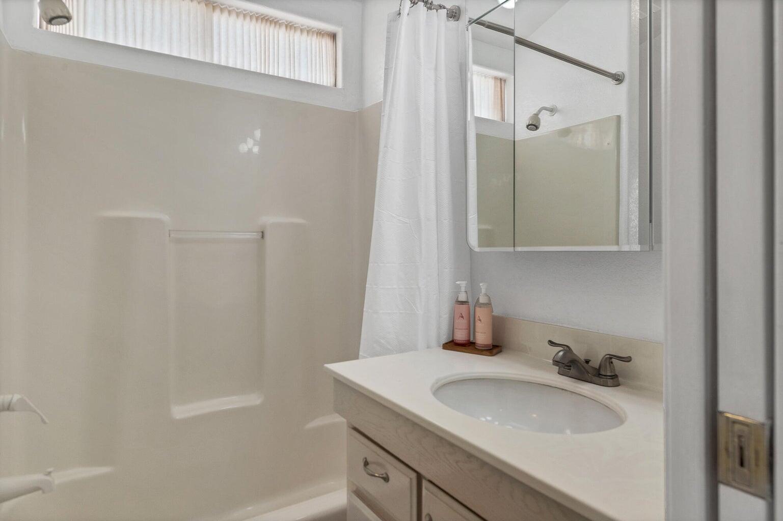 Bathroom featuring an integrated shower/tub unit with a built-in shelf, a white vanity with an undermount sink, a chrome faucet, and a mirrored medicine cabinet