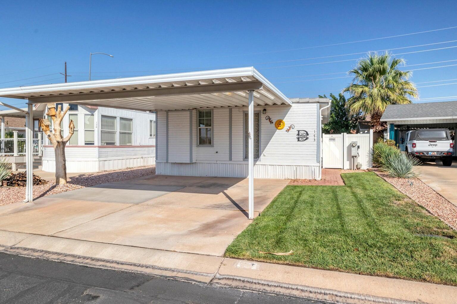 White exterior with siding, featuring a covered carport, concrete driveway, and a small lawn area