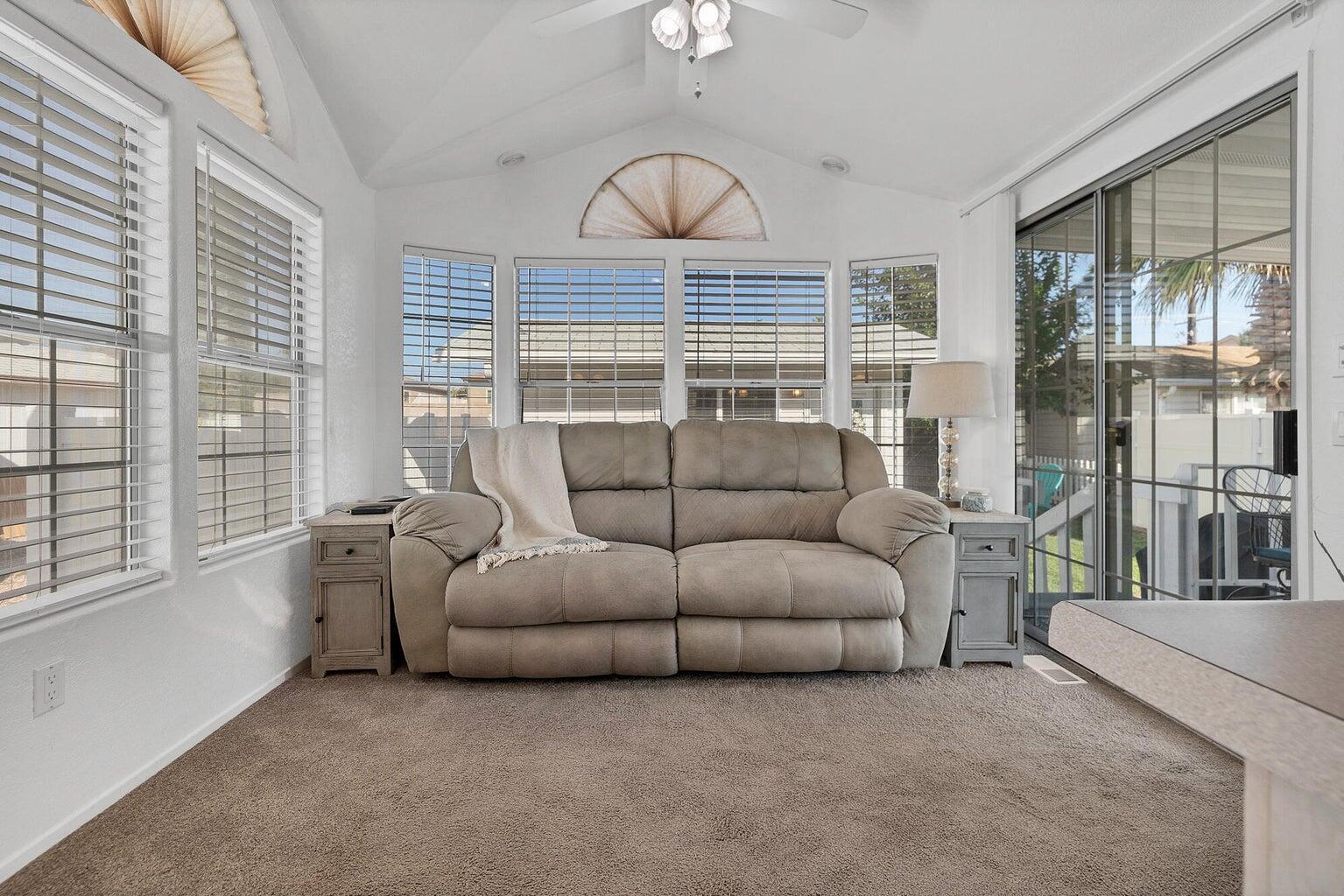 Vaulted ceiling room featuring multiple windows with blinds, a ceiling fan, and carpet flooring