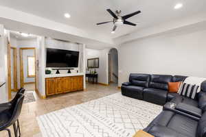 Living room with arched walkways, a ceiling fan, stone tile flooring, and recessed lighting