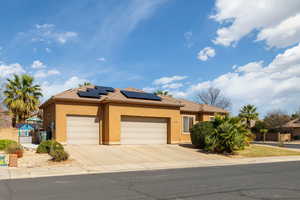 View of front of property featuring solar panels, a garage, stucco siding, and concrete driveway