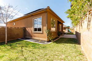 View of side of home with a fenced backyard, stucco siding, roof mounted solar panels, and a playground