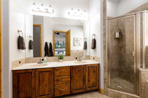 Bathroom featuring backsplash, double vanity, a shower stall, and a ceiling fan