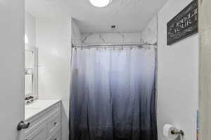Full bath featuring a shower with curtain, vanity, and a textured ceiling