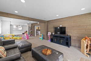 Carpeted living room with recessed lighting, beam ceiling, and wood walls