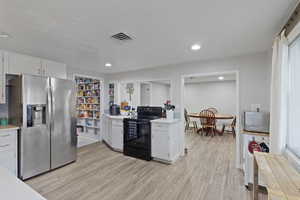 Kitchen featuring black range with electric cooktop, light countertops, stainless steel fridge, white cabinetry, and light wood-type flooring