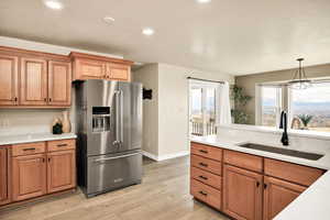 Kitchen featuring high end refrigerator, light wood finished floors, suspended lighting, light stone countertops, and wood finish cabinets