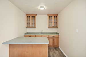 Bar with glass insert cabinets, light countertops, dark wood-style flooring, wood finish cabinetry, and a textured ceiling