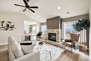 Living area with light wood-type flooring, a ceiling fan, a stone fireplace, and recessed lighting