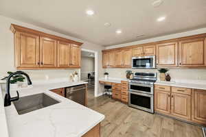 Kitchen with stainless steel appliances, light stone countertops, light wood-style flooring, recessed lighting, and wood finish cabinets