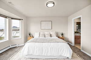 Bedroom featuring light carpet, a baseboard heating unit, and ensuite bath
