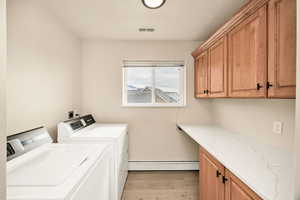 Laundry room featuring cabinet space, baseboard heating, light wood-type flooring, and independent washer and dryer