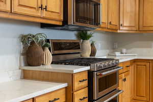 Kitchen featuring stainless steel range with gas stovetop, wood finish cabinetry, and light stone countertops