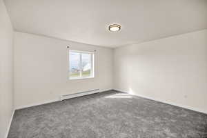 Carpeted spare room featuring a baseboard heating unit and baseboards